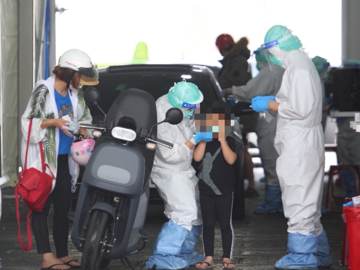 本土疫情升溫，一位家長帶著小孩騎車前往排隊(duì)篩檢。（張鎧乙攝）